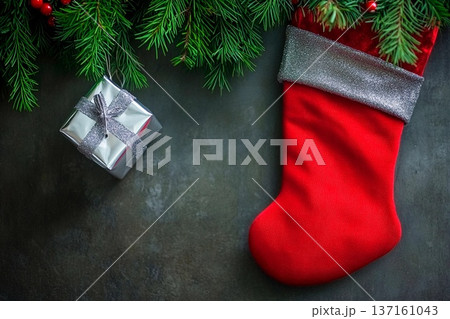 Christmas stocking and gift wrapped in silver surrounded by pine branches on a stone surface Christmas stocking and gift wrapped in silver surrounded by pine branches on a stone surface 137161043