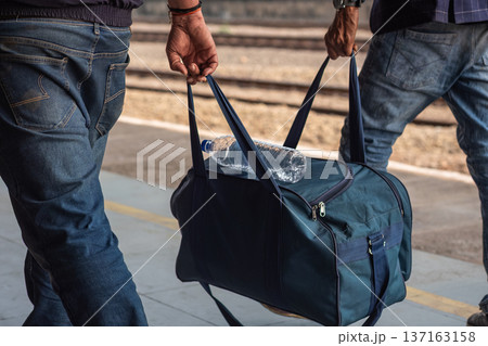 Two men carrying a heavy bag at the train station. People with travel bags walking on the station. 137163158