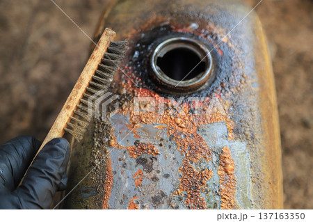 Hand using Wire Brush for cleaning old color on tank oil of motorcycle 137163350