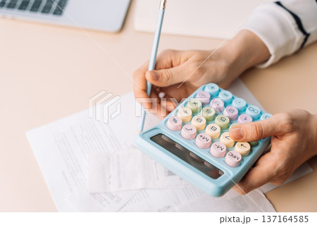Person calculating expenses with pastel calculator and pen on papers, tax and budget planning 137164585