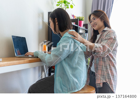 Tech-Savvy Friends: Two smiling friends, their faces illuminated by the glow of a laptop screen, collaborate on a project while relaxing comfortably on a sofa. Tech-Savvy Friends: Two smiling friends, their faces illuminated by the glow of a laptop screen, collaborate on a project while relaxing comfortably on a sofa. 137164800