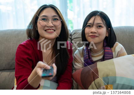 Cozy Relaxation: Two companions find comfort together on the couch, smiling while watching TV, enjoying a tranquil moment of shared leisure. Cozy Relaxation: Two companions find comfort together on the couch, smiling while watching TV, enjoying a tranquil moment of shared leisure. 137164808