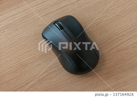 木目調のデスクに置かれた黒いワイヤレスマウス　 137164928