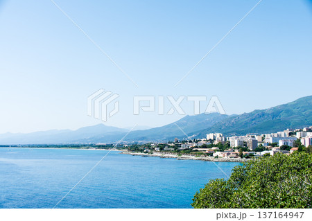 明るい日差しの下の透き通った青い海と海岸線に立ち並ぶ建物 地中海に浮かぶフランス領のコルシカ島にて 明るい日差しの下の透き通った青い海と海岸線に立ち並ぶ建物 地中海に浮かぶフランス領のコルシカ島にて 137164947