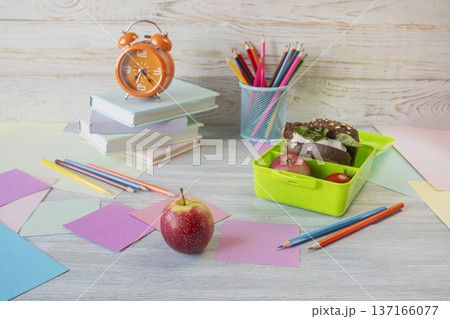 Back to school concept, school food. Lunch box with healthy sandwich, alarm clock, stack of books and apple on wooden background. Back to school concept, school food. Lunch box with healthy sandwich, alarm clock, stack of books and apple on wooden background. 137166077