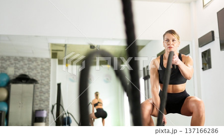 Determined woman training with battle ropes in gym Determined woman training with battle ropes in gym 137166286