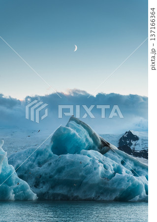 Blue iceberg floating in Jokulsarlon glacier lagoon with crescent moon in Iceland 137166364