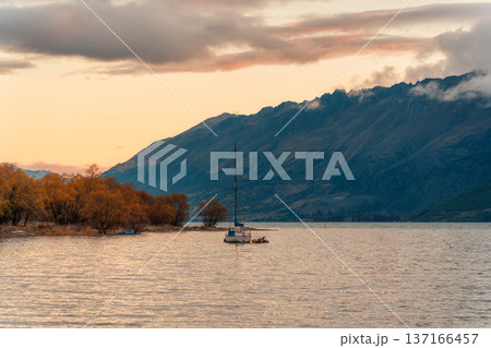Sailboat floating on calm lake with mountain and autumn forest during sunset in New Zealand Sailboat floating on calm lake with mountain and autumn forest during sunset in New Zealand 137166457