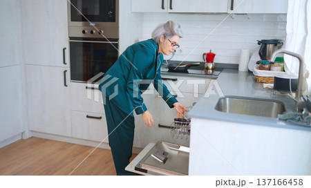 Senior woman loading dishwasher in her home kitchen Senior woman loading dishwasher in her home kitchen 137166458