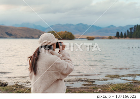 Female tourist taking a photo with compact camera on Lake Tekapo in autumn at New Zealand Female tourist taking a photo with compact camera on Lake Tekapo in autumn at New Zealand 137166622