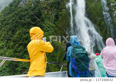 Asian woman enjoying the waterfall flowing in Milford Sound during ferry cruise on vacation Asian woman enjoying the waterfall flowing in Milford Sound during ferry cruise on vacation 137166632