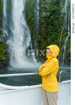 Asian woman enjoying the waterfall flowing in Milford Sound during ferry cruise on vacation Asian woman enjoying the waterfall flowing in Milford Sound during ferry cruise on vacation 137166633