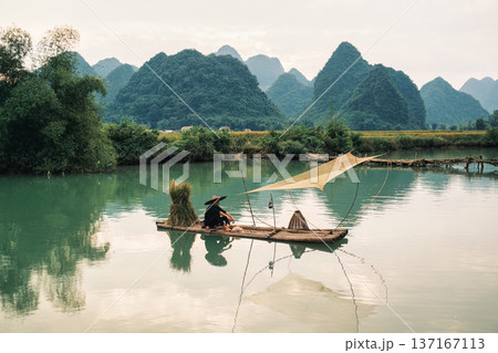 Rural scene of fisherman fishing on wooden raft, surrounded by mountain in sunny day at Phong Nam valley 137167113