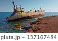 Woman standing on the rocky seashore admiring the iconic rust-covered Edro III Shipwreck grounded on the coast of Paphos, Cyprus, with clear blue Mediterranean sea and sky 137167484