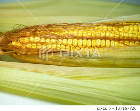 Cereal concept. Semi-husked ripe corn. Corn with leaves. Maize with hairs. Bright yellow grains. Cereal concept. Semi-husked ripe corn. Corn with leaves. Maize with hairs. Bright yellow grains. 137167720