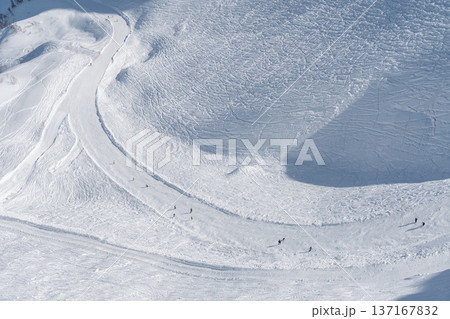 Winding ski slope on snowy mountain in Krasnaya Polyana shows groomed track with skiers descending white alpine terrain under clear winter sky, Winter tourism and outdoor sport concept for travel Winding ski slope on snowy mountain in Krasnaya Polyana shows groomed track with skiers descending white alpine terrain under clear winter sky, Winter tourism and outdoor sport concept for travel 137167832