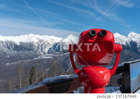 Red panoramic viewer overlooking snowy mountain range in Krasnaya Polyana stands on observation deck against blue winter sky, Travel destination concept for tourism marketing, alpine resort Red panoramic viewer overlooking snowy mountain range in Krasnaya Polyana stands on observation deck against blue winter sky, Travel destination concept for tourism marketing, alpine resort 137167849