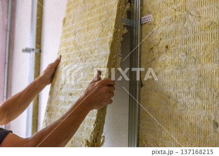 Worker insulating a room wall with mineral rock wool thermal insulation. Worker insulating a room wall with mineral rock wool thermal insulation. 137168215