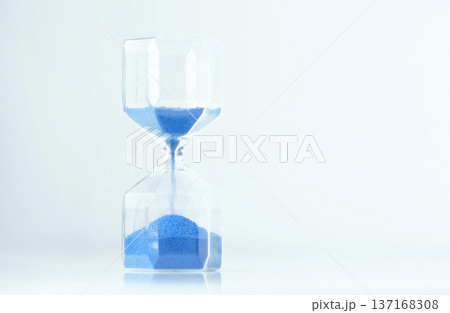Minimal timer hourglass with blue sand and empty white space, calm modern aesthetic and gentle reflections. Slow moments can reduce anxiety and support mindful living. 137168308