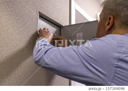 A man checks an indoor circuit breaker box A man checks an indoor circuit breaker box 137169096