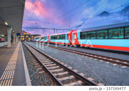Red and blue modern passenger train standing at railway station Red and blue modern passenger train standing at railway station 137169477