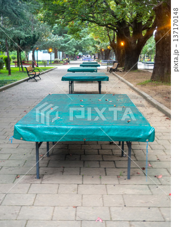 Ping pong tables covered with tarpaulin. Protect mouth from rain. End of summer concept in the park. sport in the park. holiday at the resort. Ping pong tables covered with tarpaulin. Protect mouth from rain. End of summer concept in the park. sport in the park. holiday at the resort. 137170148