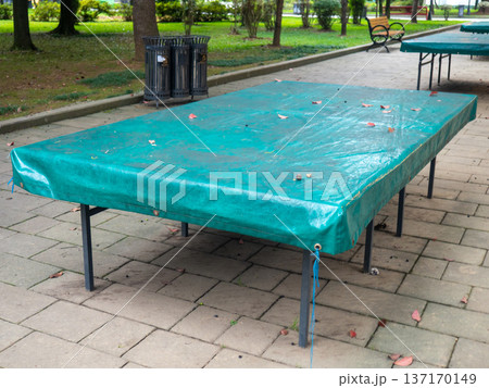 Ping pong tables covered with tarpaulin. Protect mouth from rain. End of summer concept in the park. sport in the park. holiday at the resort Ping pong tables covered with tarpaulin. Protect mouth from rain. End of summer concept in the park. sport in the park. holiday at the resort 137170149