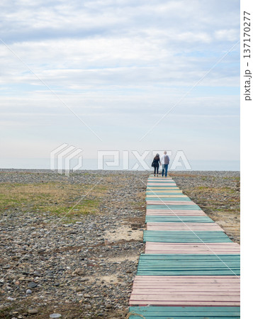 A couple holding hands walks along the path to the sea. Lovers against the backdrop of the sea. Silhouettes of people. A couple holding hands walks along the path to the sea. Lovers against the backdrop of the sea. Silhouettes of people. 137170277