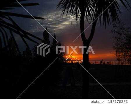 Bright sunset against the backdrop of a restaurant on the seashore. Restaurant lights. Sunset at the resort Bright sunset against the backdrop of a restaurant on the seashore. Restaurant lights. Sunset at the resort 137170278