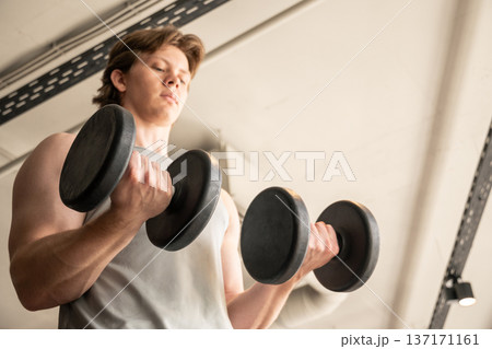 Young man doing dumbbell biceps curl in fitness club 137171161