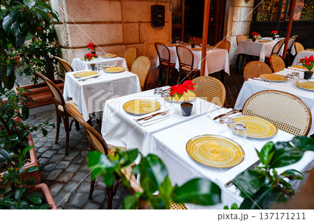 Outdoor dining area at a cafe with tables and chairs in a lively setting during the daytime 137171211
