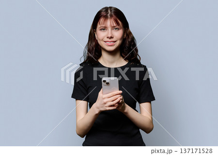 Portrait of female high school student with smartphone on gray background Portrait of female high school student with smartphone on gray background 137171528