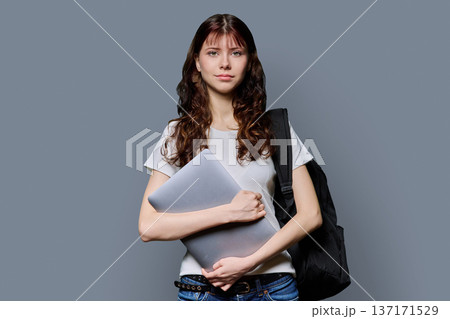 Portrait of beautiful girl teenage student with backpack, laptop on gray background 137171529