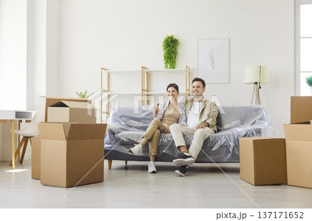 Smiling couple sitting on couch in light apartment with cardboard moving boxes Smiling couple sitting on couch in light apartment with cardboard moving boxes 137171652