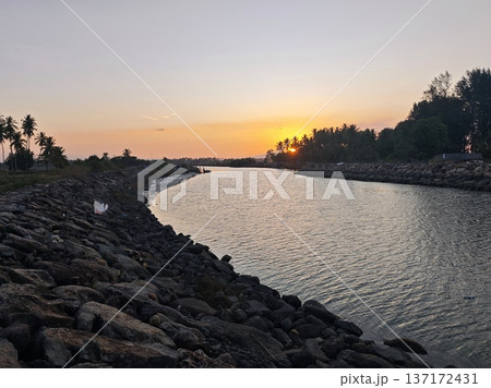 Beautiful tropical sunset over calm river channel bordered by rocks Beautiful tropical sunset over calm river channel bordered by rocks 137172431
