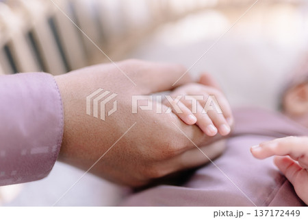 Parent's warm hand gently holds tiny newborn baby fingers in affection Parent's warm hand gently holds tiny newborn baby fingers in affection 137172449