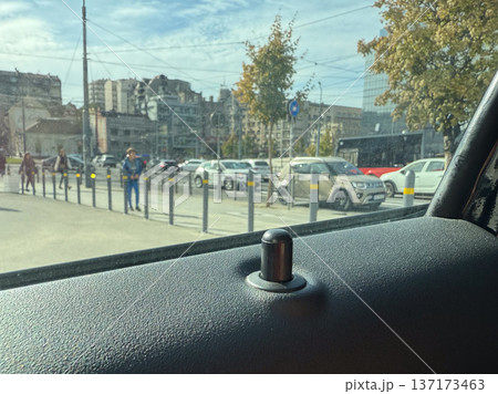 Car door lock pin with street view outside window close-up. Urban environment, transportation security and everyday mobility in city surroundings. 137173463
