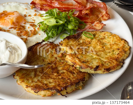 Potato pancakes with sour cream and onion on plate close-up. Traditional meal, homemade flavor, and cozy rustic breakfast. Potato pancakes with sour cream and onion on plate close-up. Traditional meal, homemade flavor, and cozy rustic breakfast. 137173464