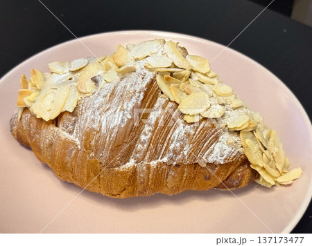 Golden croissants topped with almond slices and powdered sugar on plate close-up. Classic pastry presenting bakery tradition, sweetness, and flaky layered texture. 137173477