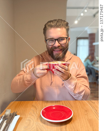 Man enjoying latte in modern cafe. Everyday relaxation, morning ritual and cozy coffee culture in urban lifestyle setting. 137173487