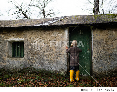 Back view of girl in yellow boots looking at entrance of stone building 137173513