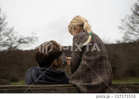 Little girl and boy sharing mobile device while sitting in autumn park Little girl and boy sharing mobile device while sitting in autumn park 137173518