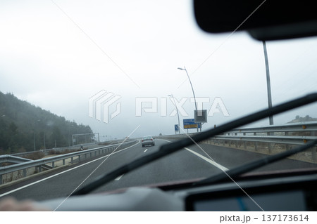 View through the windshield of a car moving along a misty motorway with traffic signs and low visibility 137173614