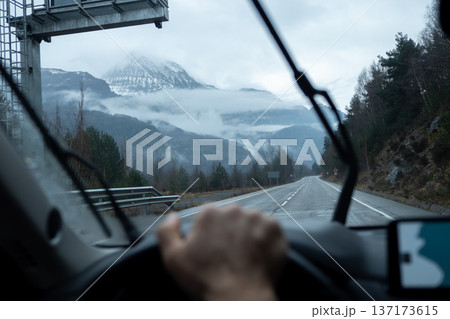 Steering wheel and dashboard visible while driving on an open road toward misty alpine summits 137173615