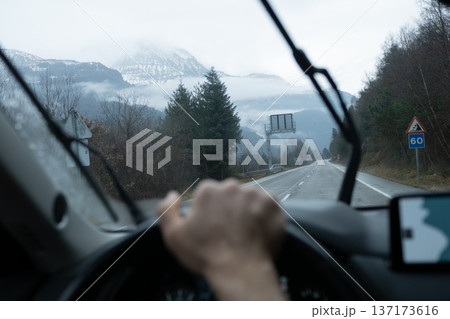 Driving on a straight road toward distant mountains covered in snow and low hanging clouds on a dull day 137173616