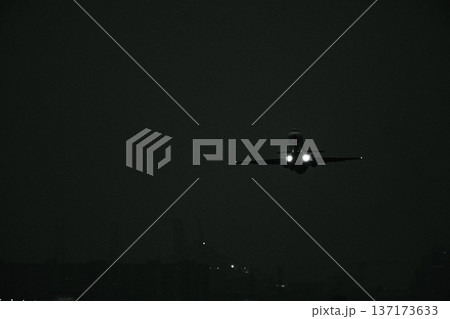 Monochrome view of a commercial jet aircraft approaching the runway with illuminated headlights in complete darkness Monochrome view of a commercial jet aircraft approaching the runway with illuminated headlights in complete darkness 137173633
