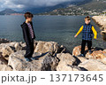 Two boys balancing on rocks by sea, childhood adventure, risk and exploration in coastal mountain landscape 137173645