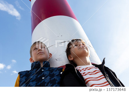 Two boys under lighthouse looking up, childhood dreams, future and direction, coastal lifestyle. Low angle 137173648