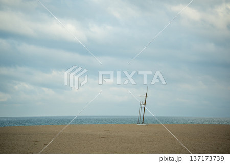 Minimalist view of a tall lifeguard chair standing on a sandy beach under a cloudy sky 137173739