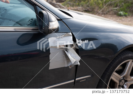 Close up view of black car door with body damage covered by messy silver duct tape Close up view of black car door with body damage covered by messy silver duct tape 137173752